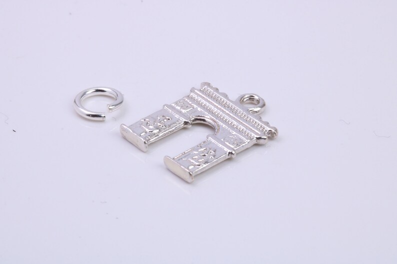 May include: Silver charm in the shape of the Arc de Triomphe, a famous Parisian landmark. The charm has a jump ring attached for easy attachment to a necklace or bracelet.