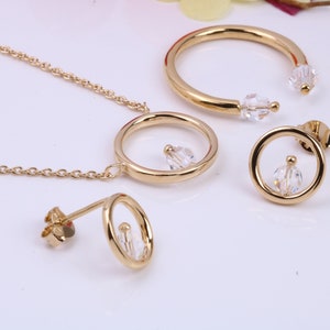 May include: A gold necklace with a circle pendant and a crystal charm. The set also includes a pair of matching earrings with circle pendants and crystal charms.