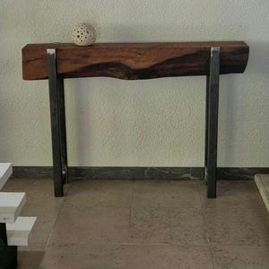 Op de afbeelding: Een rustieke houten consoletafel met een live edge blad en zwarte metalen poten. De tafel is gemaakt van gerecycled hout en heeft een natuurlijke afwerking.