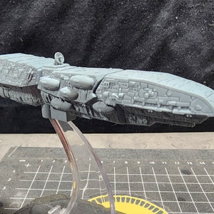 May include: A gray, detailed, 3D printed model of a spaceship on a clear plastic stand. The spaceship has a long, cylindrical body with a rounded nose and a variety of small details.