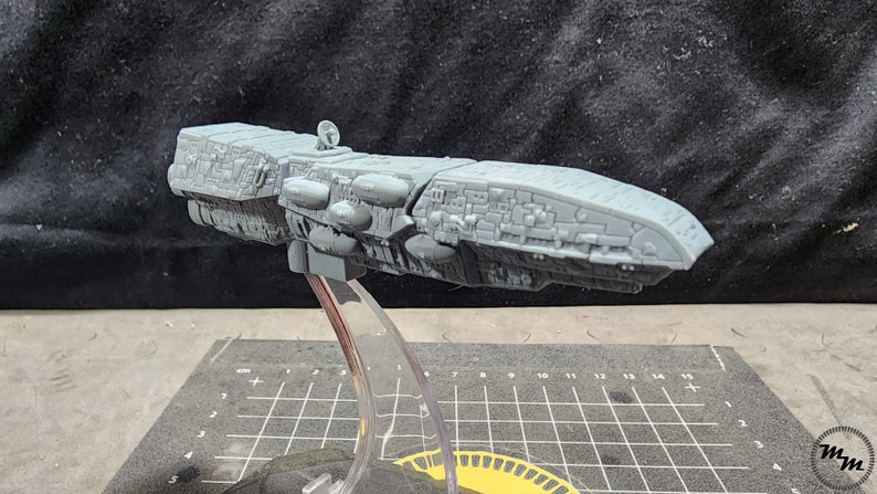 May include: A gray, detailed, 3D printed model of a spaceship on a clear plastic stand. The spaceship has a long, cylindrical body with a rounded nose and a variety of small details.
