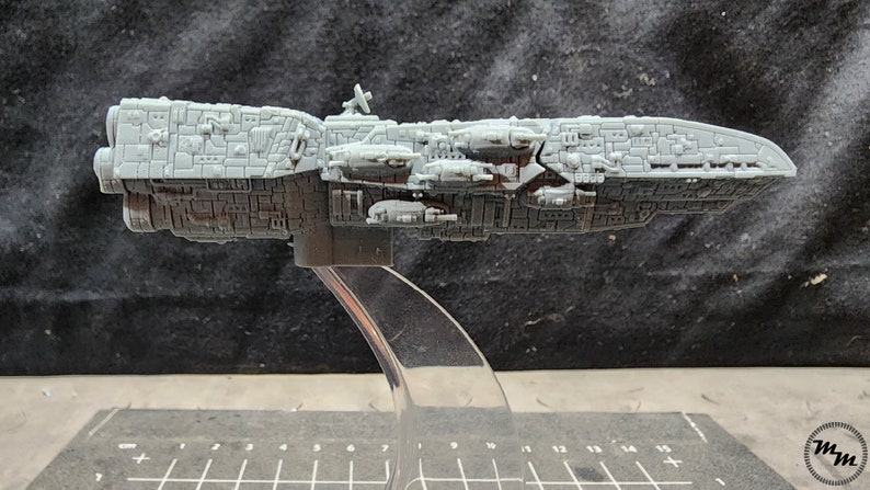 May include: A gray, detailed model of a large spaceship with a long, narrow body and multiple smaller ships attached to the side. The model is on a clear plastic stand.