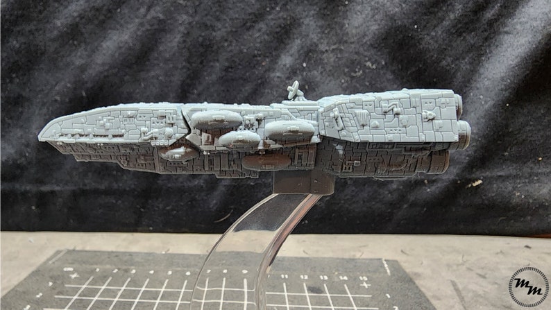 May include: A gray, detailed model of a spaceship with a rounded front and a long, rectangular body. The spaceship has several small, round pods attached to the side and a small, round antenna on top.