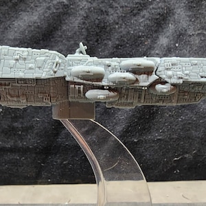 May include: A gray, detailed model of a spaceship with a long, cylindrical body and multiple round pods on the side. The model is on a clear plastic stand.
