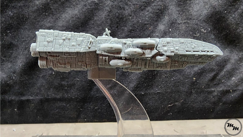 May include: A gray, detailed model of a spaceship with a long, cylindrical body and multiple round pods on the side. The model is on a clear plastic stand.