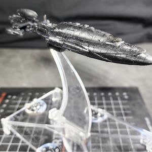 Op de afbeelding: Een zwart, gedetailleerd model van een ruimteschip op een transparante plastic standaard. Het model is gemaakt van een getextureerd materiaal en heeft een strak, futuristisch ontwerp.