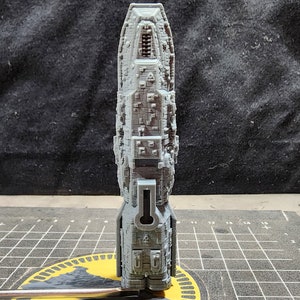 May include: A gray, detailed, 3D printed model of a spaceship. The model is standing on a gray and yellow cutting mat.