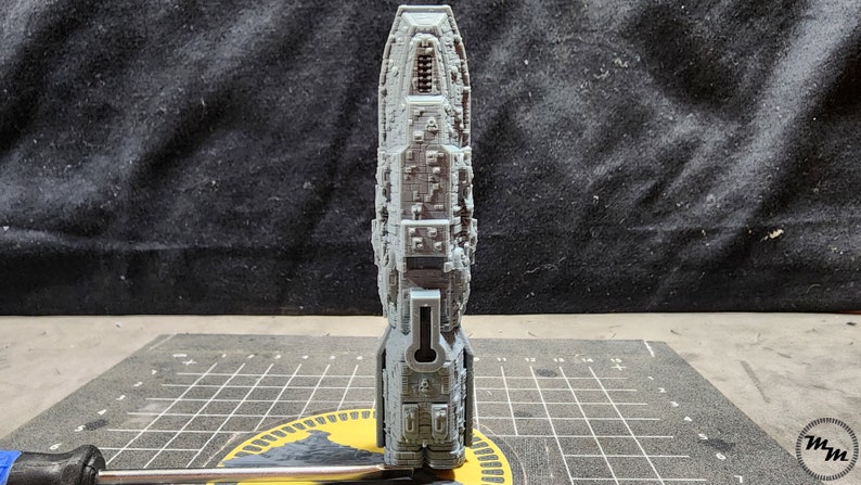May include: A gray, detailed, 3D printed model of a spaceship. The model is standing on a gray and yellow cutting mat.