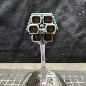 May include: A gray model of a spaceship with a cluster of eight brown exhaust ports on the back. The model is mounted on a clear plastic stand.