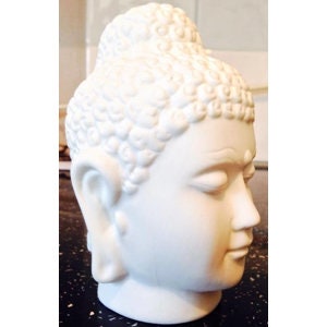May include: White ceramic Buddha head sculpture with a detailed hairstyle and serene facial expression.