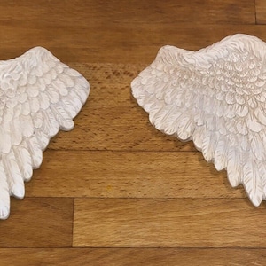 May include: A pair of white, decorative angel wings with a detailed feather design. The wings are made of a lightweight material and are perfect for adding a touch of whimsy to any space.