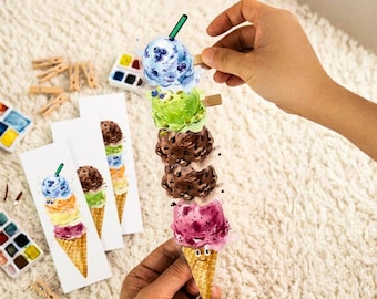 May include: A vertical bookmark featuring a watercolor illustration of a tall ice cream cone with five stacked scoops in shades of blue, green, brown, and pink, topped with a green straw, alongside several identical bookmarks and wooden clips.