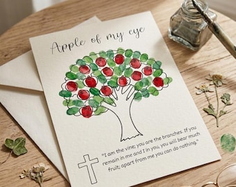 May include: A white greeting card featuring a black line drawing of a tree with red fingerprint apples and green fingerprint leaves. The text reads Apple of my eye and I am the vine; you are the branches. If you remain in me and I in you, you will bear much fruit; apart from me you can do nothing. A black cross is also printed.