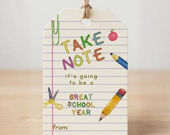 May include: A rectangular paper gift tag with a lined notebook paper pattern, featuring a jute twine loop. The text reads TAKE NOTE it's going to be a GREAT SCHOOL YEAR from. Illustrations include a green paperclip, red apple, blue pencil, yellow scissors, and a yellow pencil.