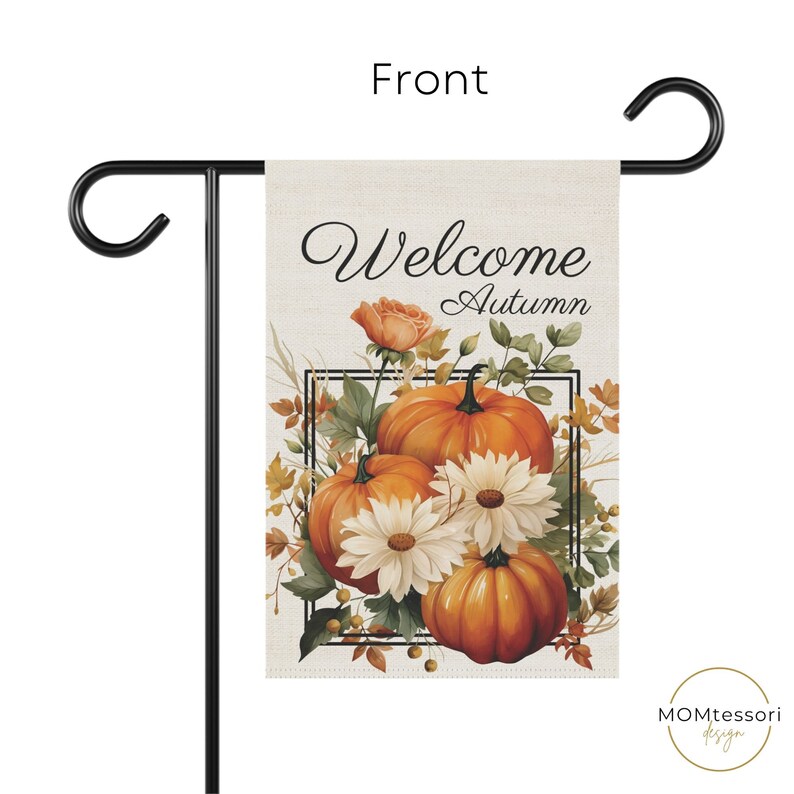 A garden flag with the words "Welcome Autumn" in elegant script. The flag features a watercolor design of pumpkins, white daisies, and fall foliage. The flag is displayed on a black metal stand.