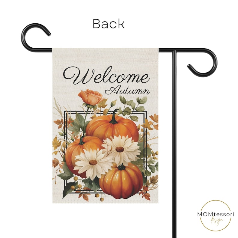 A rectangular garden flag with a black metal stand. The flag features the second side with words "Welcome Autumn" above a watercolor illustration of pumpkins, white daisies, and fall foliage. The flag is beige.