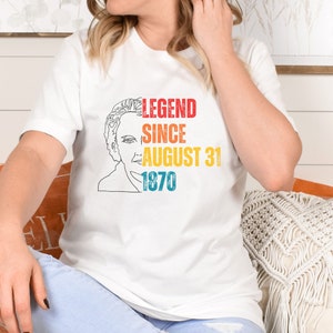 May include: A white short-sleeved t-shirt featuring a black line-art portrait of a person on the left side. To the right, the text reads LEGEND in red, SINCE in orange, AUGUST 31 in yellow, and 1870 in blue, all in a distressed, block-style font.