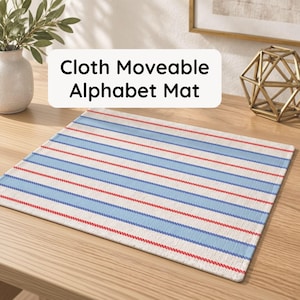 May include: A rectangular cloth moveable alphabet mat featuring a repeating pattern of wide light blue stripes and thin red stripes on an off-white background. The text Cloth Moveable Alphabet Mat is printed in black on a white rectangular overlay.