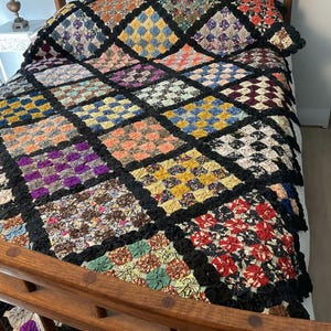 May include: A bed quilt constructed from numerous small fabric yo-yos arranged in a diamond pattern. Each diamond block features a distinct color palette, including red, yellow, blue, purple, and brown, all bordered by a black fabric lattice.