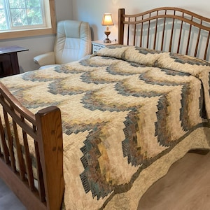 Könnte beinhalten: Ein hölzernes Bettgestell mit einer gemusterten Steppdecke. Die Steppdecke weist ein sich wiederholendes Design in Beige-, Grün- und Brauntönen auf. Das Bettgestell ist aus hellbraunem Holz gefertigt und hat ein Kopfteil mit vertikalen Lamellen.