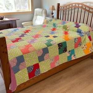 May include: A wooden bed frame with a colorful quilt. The quilt features a green background with various square patches in shades of red, pink, blue, and yellow. The bed frame is made of light brown wood.