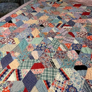 May include: A patchwork quilt featuring a multitude of diamond-shaped fabric pieces in various colors and patterns, including floral, plaid, polka dot, and striped designs. The quilt is stitched together with visible quilting lines throughout.