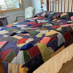 May include: A patchwork quilt with a variety of fabric pieces in shades of blue, red, green, and pink. The quilt is on a wooden bed frame with a white bed skirt. The quilt's design is a mix of geometric shapes.