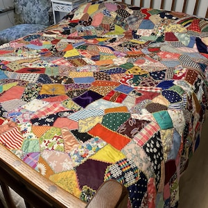 May include: A patchwork quilt featuring a chaotic arrangement of multi-colored fabric scraps in various shapes and sizes. The quilt displays a wide array of patterns, including florals, stripes, polka dots, and solid colors, joined together with visible stitching.