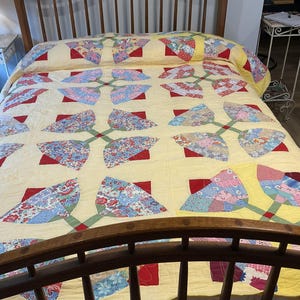 May include: A handmade quilt with a yellow background and a floral pattern. The quilt features red, blue, and white floral designs, connected by green stems. The quilt is on a wooden bed frame.