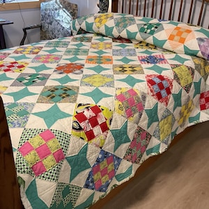 May include: A patchwork quilt featuring a repeating pattern of multi-colored fabric squares in various prints and solid colors, interspersed with teal four-pointed star shapes. The quilt is constructed with white fabric borders between the blocks.