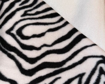 May include: Close-up of a fabric with a zebra print pattern. The fabric features bold black stripes against a white background. The image also shows a solid white fabric, creating a contrast in textures and colors.