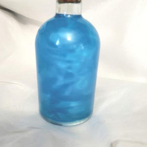 Könnte beinhalten: Eine Glasflasche mit einem Korkverschluss, gefüllt mit einer schimmernden blauen Flüssigkeit.