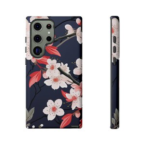 May include: A phone case with a dark blue background and a floral pattern of pink and white cherry blossoms and red leaves.
