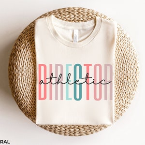 May include: A white t-shirt with the text "DIRECTOR athletic" in colorful vertical stripes. The text is in a modern font style.