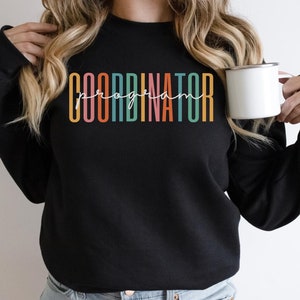 May include: Black sweatshirt with the text "program coordinator" in rainbow colors.
