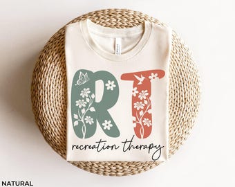 Op de afbeelding: Een wit T-shirt met de letters RT in groen en rood met bloemmotieven. De tekst "recreation therapy" staat onder de letters.
