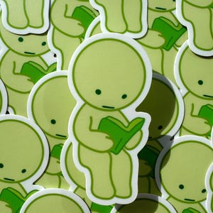 May include: A collection of green and white stickers featuring a simple cartoon character reading a book. The character has a round head, small eyes, and a small mouth. The stickers are all different sizes and are arranged in a random pattern.