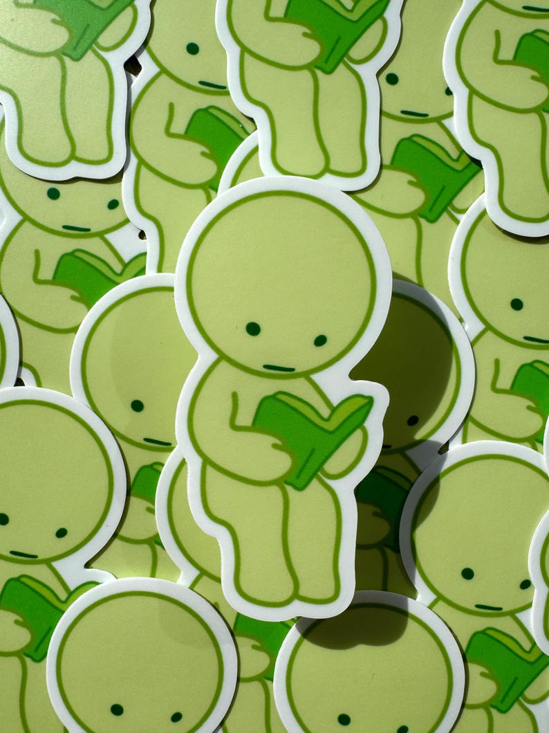 May include: A collection of green and white stickers featuring a simple cartoon character reading a book. The character has a round head, small eyes, and a small mouth. The stickers are all different sizes and are arranged in a random pattern.