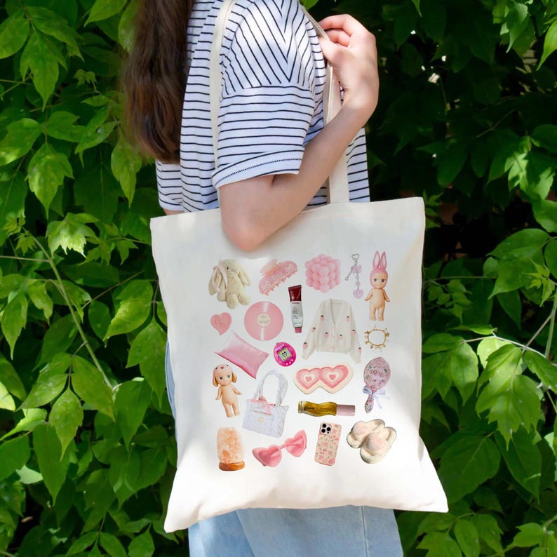 May include: A white tote bag with a pink and white design featuring various items, including a pink heart, a pink bunny, a pink phone, a pink record, a pink pillow, a pink hair clip, a pink lip balm, a pink doll, a pink ring, a pink flower, a pink lamp, a pink bow, a pink perfume bottle, a pink heart-shaped sunglasses, and a pink and white bag.