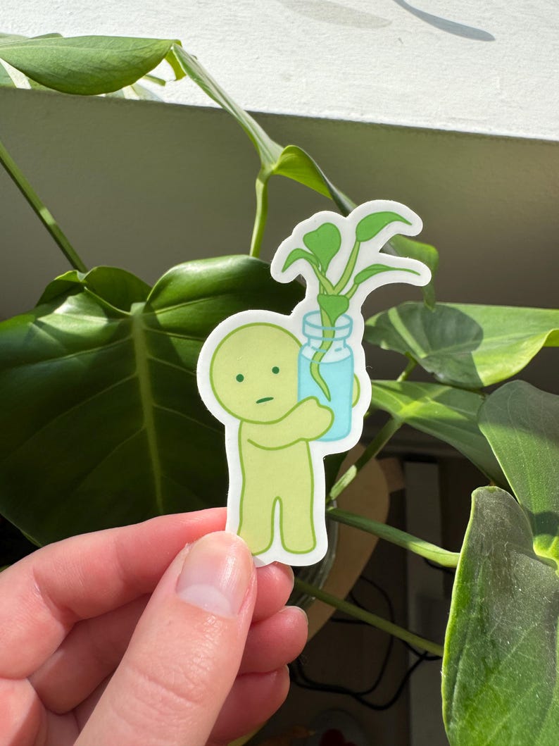 May include: A green cartoon character holding a glass jar with a small green plant inside. The character has a simple, round face with a single eye and a small mouth.