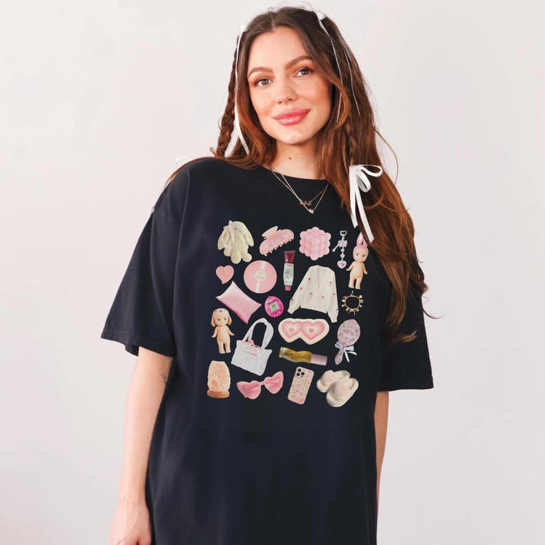 May include: A black t-shirt with a graphic print of various pink and white items, including a doll, a heart, a purse, a phone, and a pair of slippers.