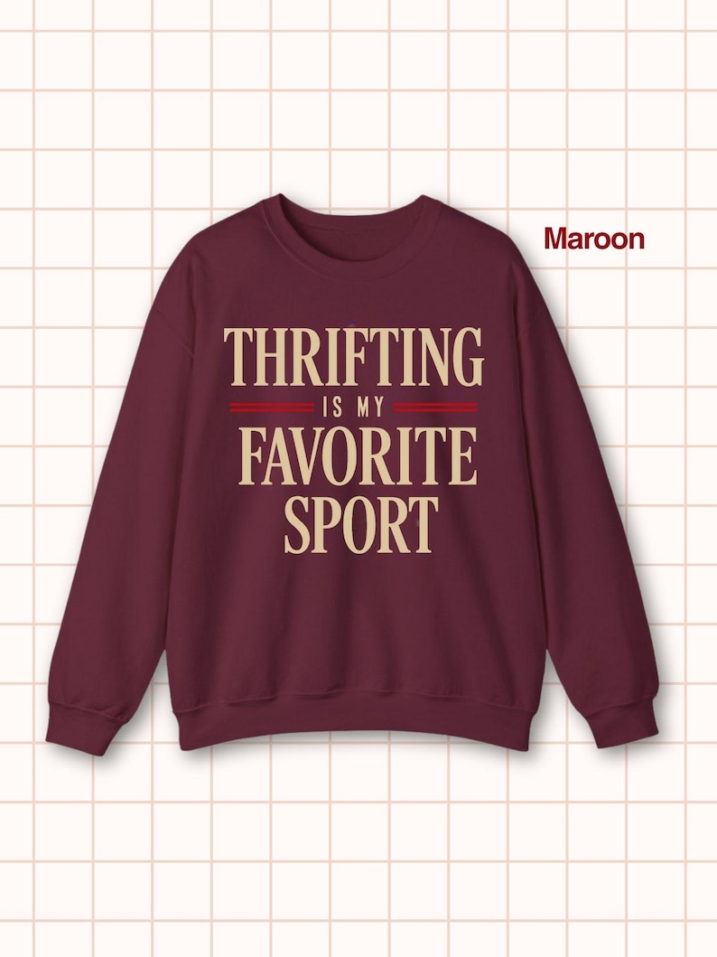 May include: Maroon crewneck sweatshirt with the text "Thrifting is my favorite sport" in a cream-colored font. The text is centered on the front of the sweatshirt, with two red lines separating the phrases. The sweatshirt is a solid maroon color.