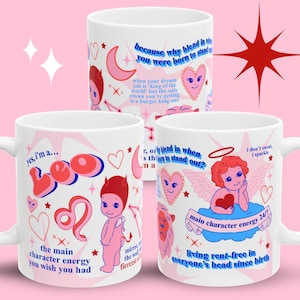 May include: White ceramic mug with a pink and blue design featuring the zodiac sign Leo. The mug has text that reads "yes, I'm a... Leo" and "the main character energy you wish you had".