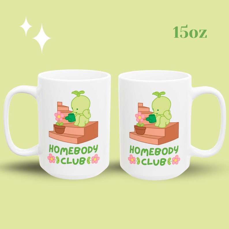 May include: Two white ceramic mugs with a whimsical design. Each mug features a green cartoon character watering a flower on a brown structure, with the text "HOMEBODY CLUB" and a flower graphic. The mugs are labeled "15oz".