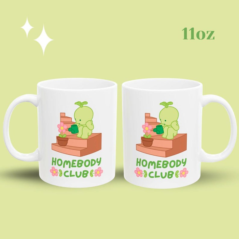 May include: Two white ceramic mugs with a whimsical illustration of a green character watering a flower on a set of steps. The mugs have the text "HOMEBODY CLUB" and are 11oz.