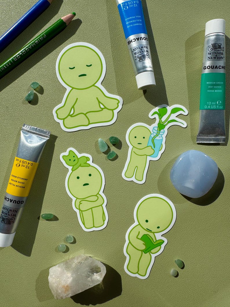 May include: Five green stickers featuring cartoon characters with different expressions. The characters are all wearing green clothing and have a simple design. The stickers are on a green background with small green and blue stones.