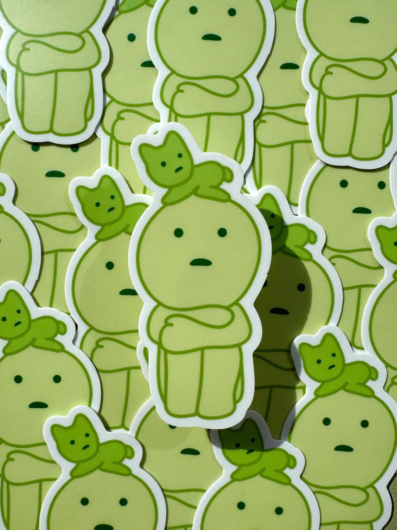 May include: A collection of green stickers featuring a cartoon character with a cat on its head. The character has a simple design with a round head, arms crossed, and legs. The cat is also simple, with a round head, ears, and a tail.