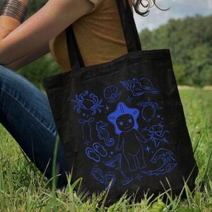 May include: Black tote bag with blue illustrations of sea creatures, including a crab, starfish, seahorse, and seashells. The bag has two black handles and is made of a sturdy fabric. The design is whimsical and nautical-themed.