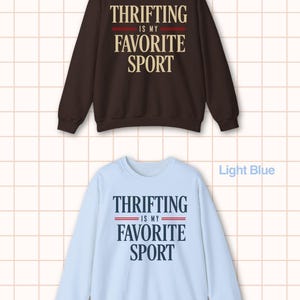 May include: Two sweatshirts, one dark chocolate and one light blue, each with the text "THRIFTING IS MY FAVORITE SPORT" in a bold, sans-serif font. The text is centered, with a red stripe above the words "FAVORITE SPORT".
