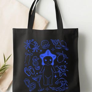 May include: Black tote bag with a blue illustration of beach-themed elements. The design includes a crab, seashells, a starfish-headed figure, a seahorse, flip-flops, a cocktail, and a wave.